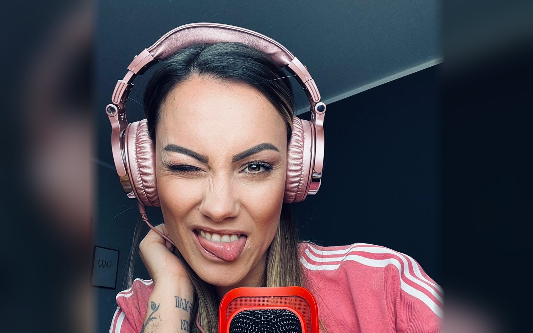 Stephy mit rosa Kopfhörern am Podcast-Mikrofon, zwinkernd