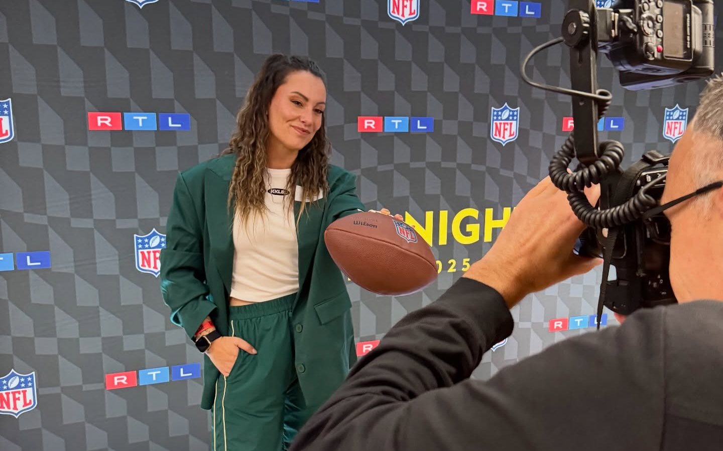 Stephy mit Football vor einer NFL-Fotowand, ein Fotograf fotografiert sie